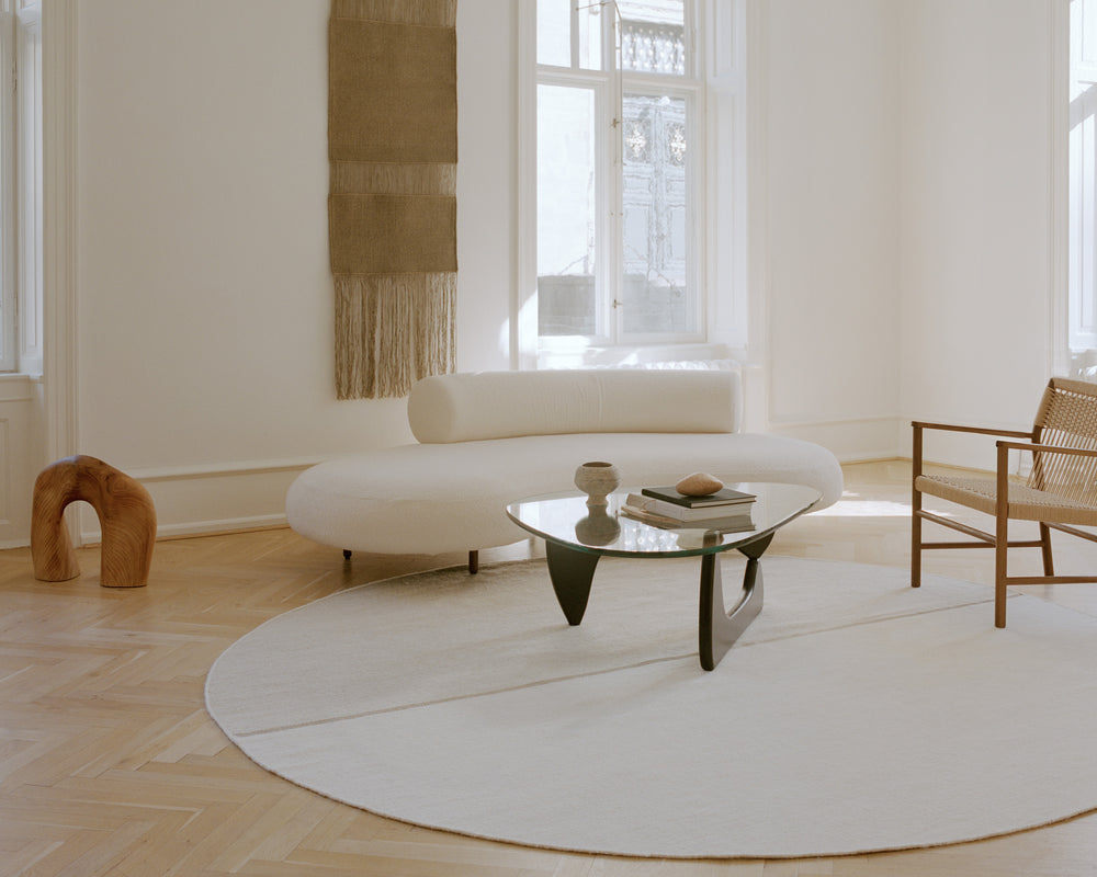 Modern living room with a white sofa, round coffee table, and wooden chair.